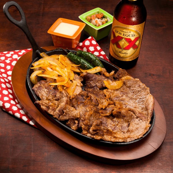 Sizzling fajita meat with onions and peppers in a cast iron skillet, with Dos Equis beer.