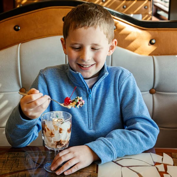 Smiling boy in a blue shirt enjoying a chocolate sundae with a cherry at El Vaquero.
