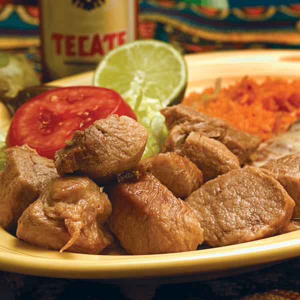 El Vaquero's Mexican dish with cubed meat, rice, tomato, lettuce, and lime, with a Tecate beer in the background.