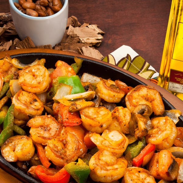 Sizzling shrimp fajitas with bell peppers and onions, served with a side of beans.