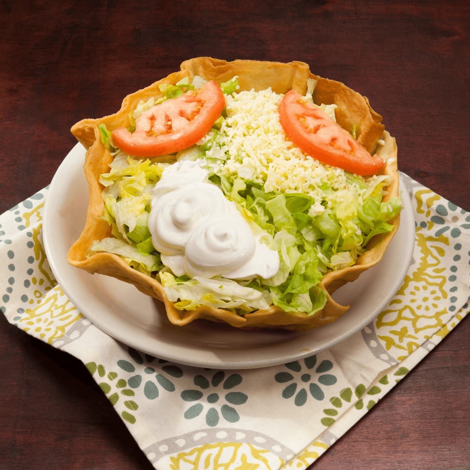 El Vaquero taco salad with lettuce, shredded cheese, tomatoes, and sour cream in a crispy shell.