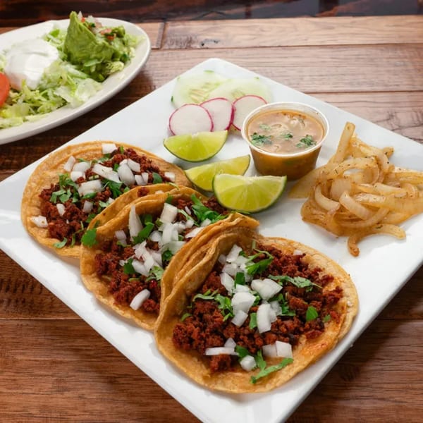Three El Vaquero tacos with meat, onions, cilantro, limes, soup, and a side salad.