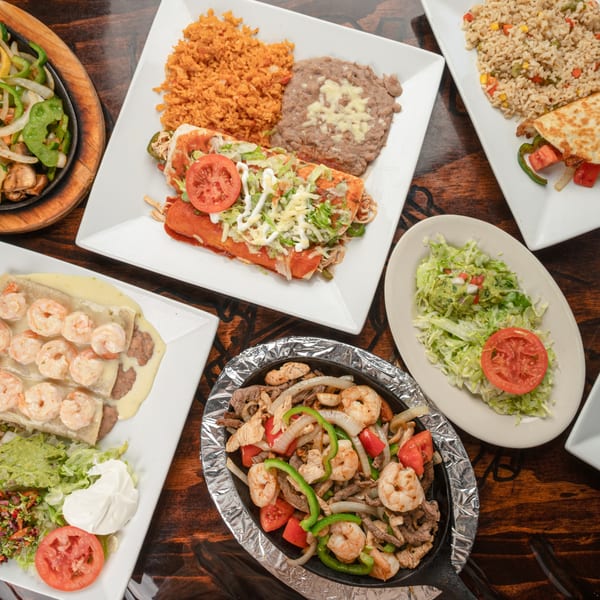 Overhead view of various Mexican dishes, including enchiladas, fajitas, and shrimp burritos, on a wooden table.