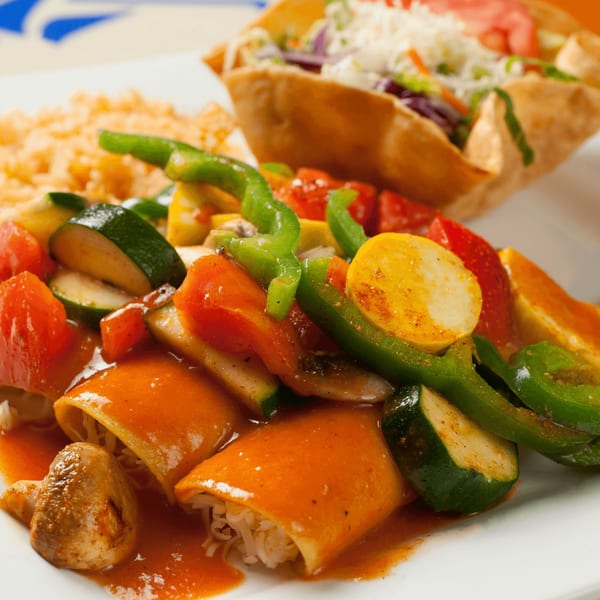 El Vaquero's enchiladas with rice, sautéed vegetables, and a taco salad in the background.