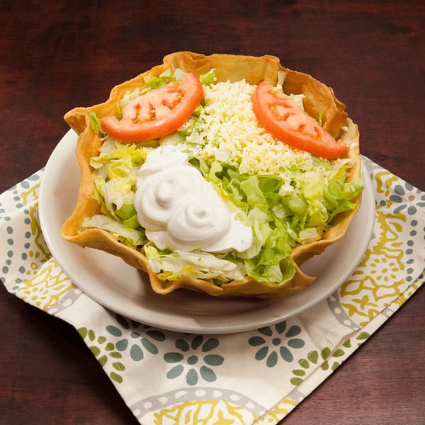 El Vaquero taco salad in a crispy shell with lettuce, cheese, tomatoes, and sour cream.