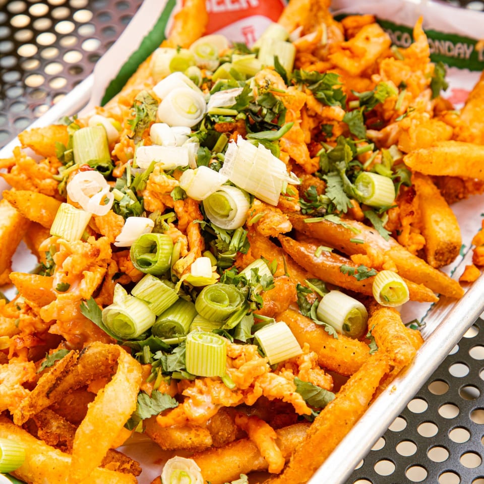 El Vaquero's loaded fries, topped with cheese, green onions, and cilantro, served in a metal tray.