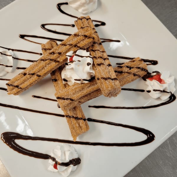 El Vaquero churros with chocolate drizzle, whipped cream, and strawberry sauce on a white plate.