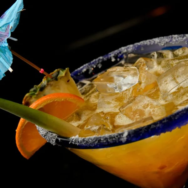 El Vaquero's margarita with ice, orange slice, pineapple, and a blue umbrella.